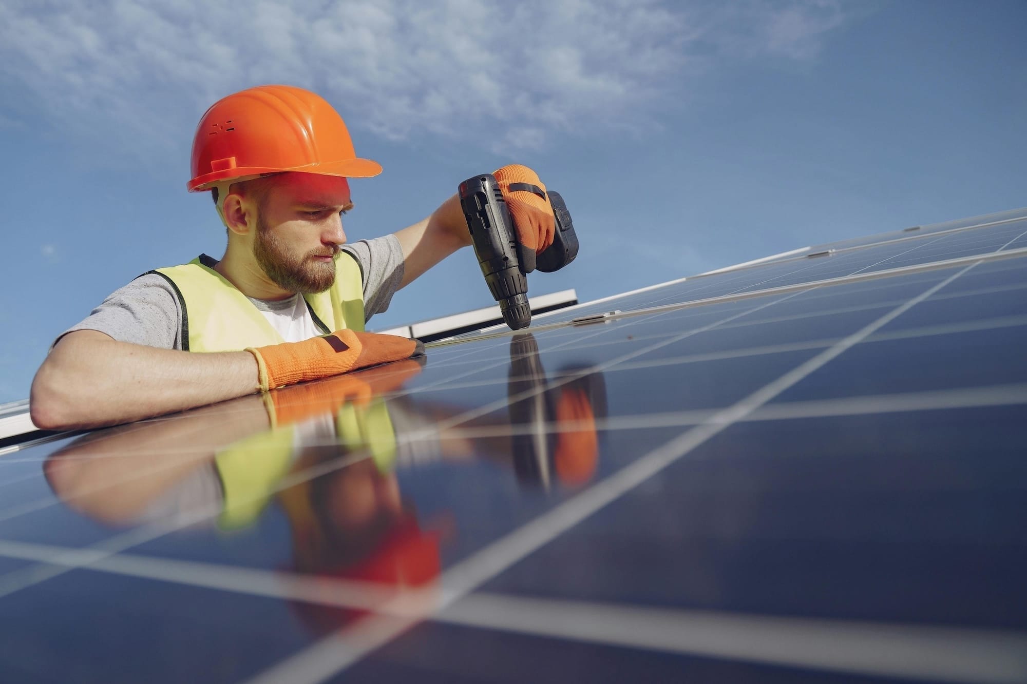 Ein junger Mann mit einem Bauhelm montiert ein PV-Modul