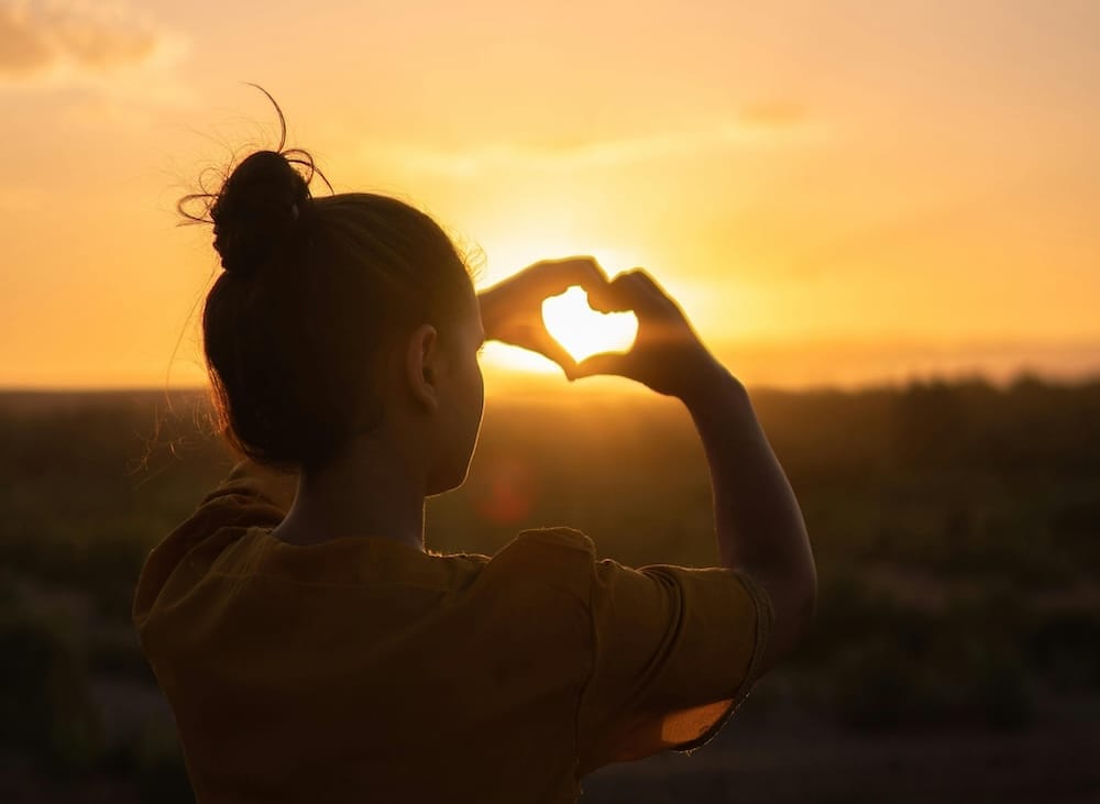 Eine junge Frau formt ein Herz mit ihren Händen und die Sonne scheint hindurch Eine junge Frau formt ein Herz mit ihren Händen und die Sonne scheint hindurch