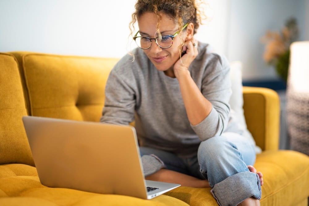Eine junge Frau surft mit ihrem Notebook im Internet und sitzt dabei gemütlich auf der Couch Eine junge Frau surft mit ihrem Notebook im Internet und sitzt dabei gemütlich auf der Couch